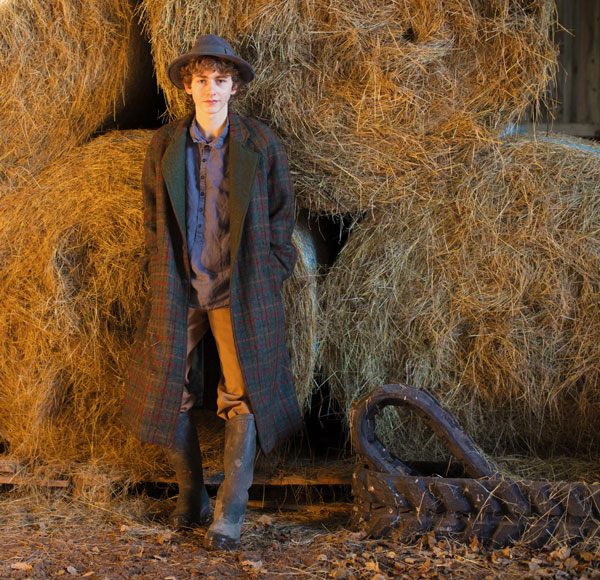long harris tweed coat modeled by young man in barn next to some hay